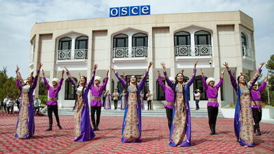 Traditional dancers in colorful attire performing in front of an OSCE building.