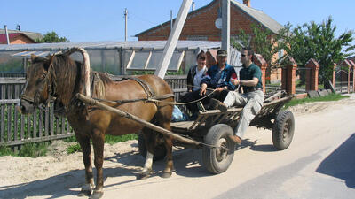 People on horse-drawn cart riding along a village street.