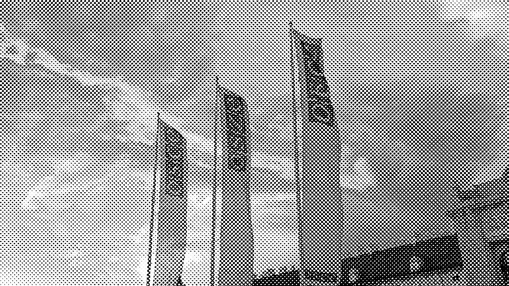 Flags with the "OSCE" logo wave in front of a historic building at sunset, with a colorful sky and people walking nearby.
