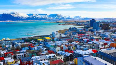 Colorful Reykjavik buildings, with a coastal view and snow-capped mountains in the background.