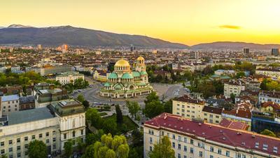 Aerial view of Sofia at sunset, with Alexander Nevsky Cathedral and mountain backdrop.