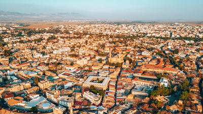 Aerial view of Nicosia, Cyprus with dense buildings and roads, set against a mountainous horizon under a clear blue sky.