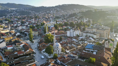 Aerial view of a town with a mosque, surrounded by hills and buildings, under a clear sky.