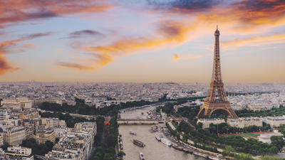 Paris skyline with the Eiffel Tower at sunset, colorful sky, and the Seine River winding through the city.