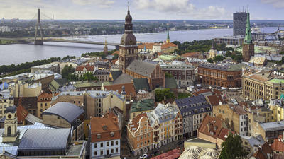 Aerial view of a European city with colorful buildings, a river, and a distant bridge under a blue sky.