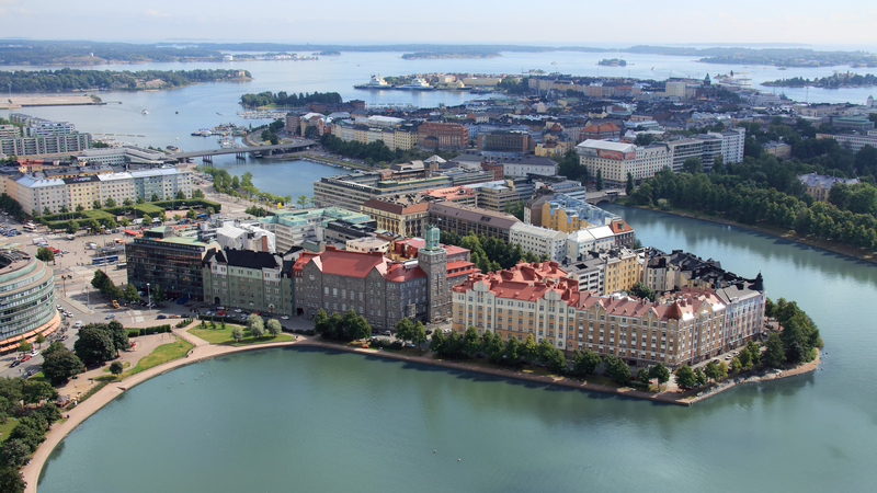 Aerial view of Helsinki Congress Paasitorni, surrounded by water, colorful buildings, and cityscape under a clear blue sky.